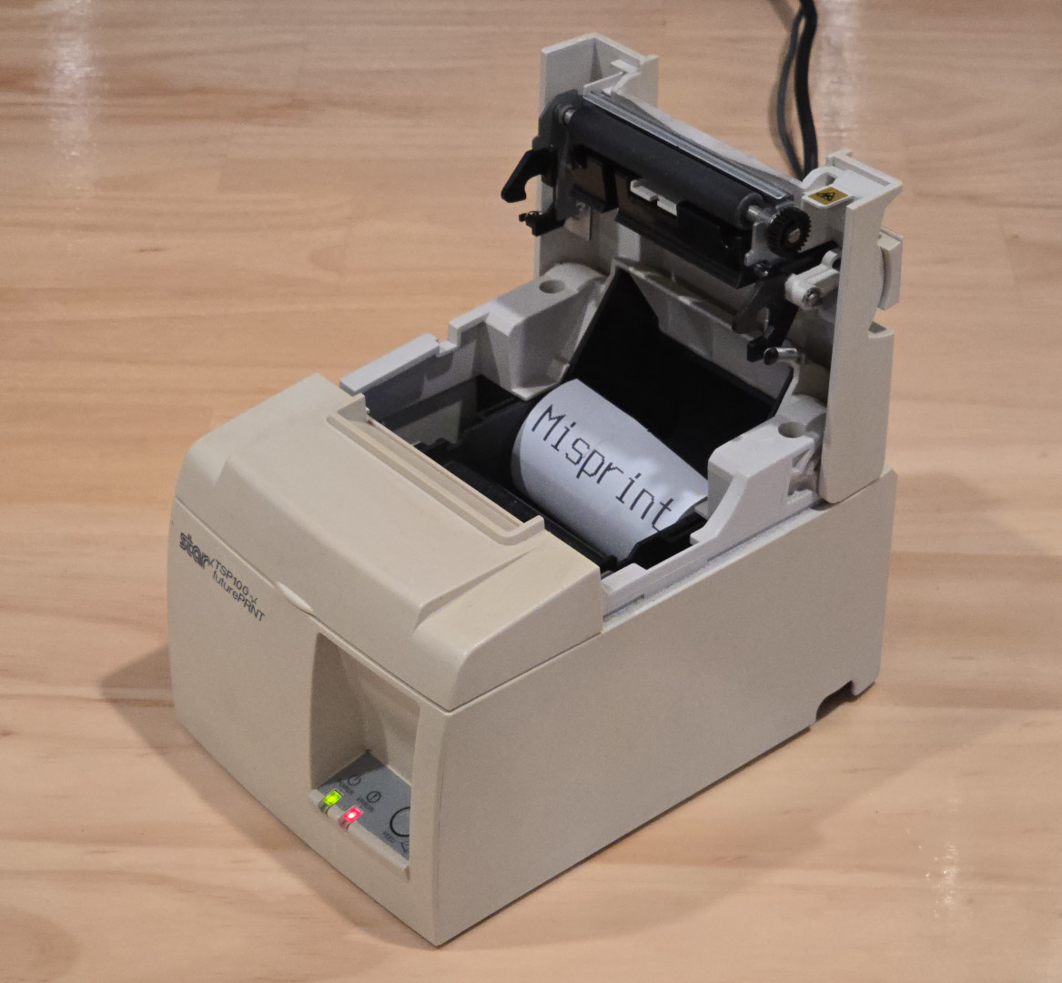 A photo of the Star Micronics TSP100 printer with its maintenance hatch open and a roll of receipt paper spooled up inside of it with the text "Misprint" printed on it.